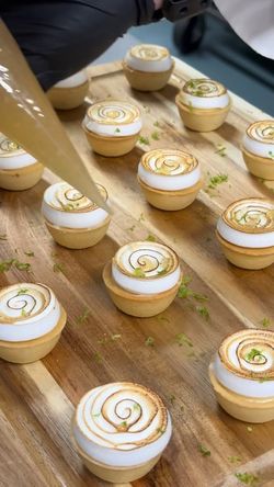 Mini tarts with toasted meringue swirls being decorated on a wooden board, showcasing luxury catering desserts.