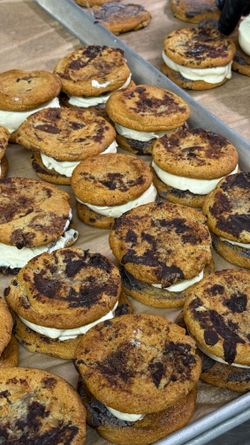 Chocolate chip cookie sandwiches with cream filling arranged on a tray in a catering kitchen.