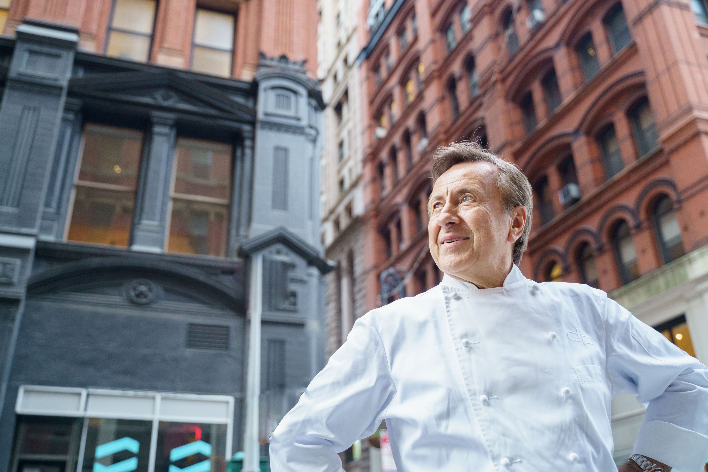 Renowned chef Daniel Boulud stands confidently outside a historic building in New York City.
