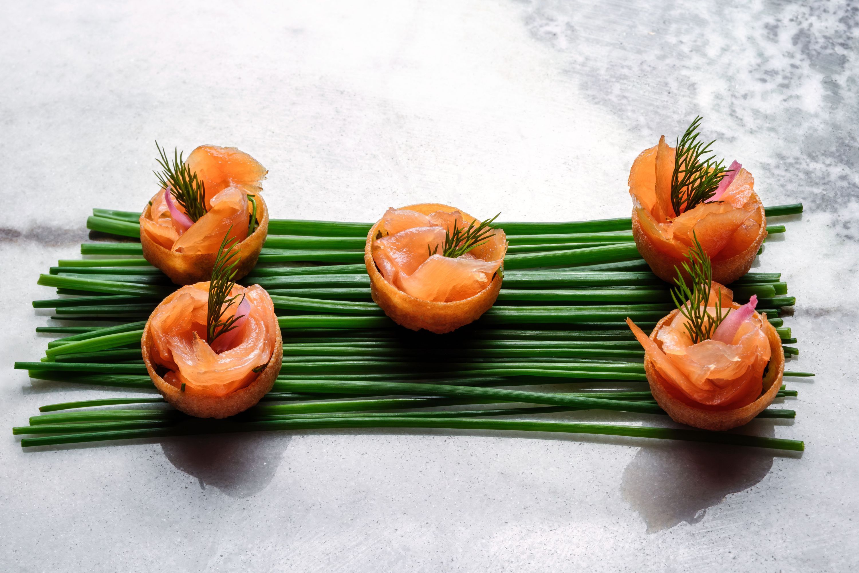 Delicate salmon tartare presented in crispy cups with fresh chives, showcasing an upscale catering option.