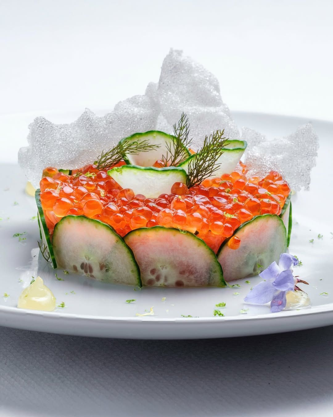 A beautifully plated dish featuring a layer of cucumber, topped with vibrant salmon roe and garnished with delicate herbs.